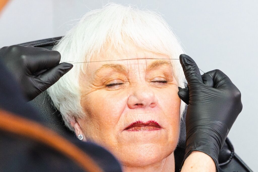 Close-up of a patient closing her eyes as a provider uses thread to mark her eyebrow shape. This step happens before the artist provides permanent cosmetics in Myrtle Beach.